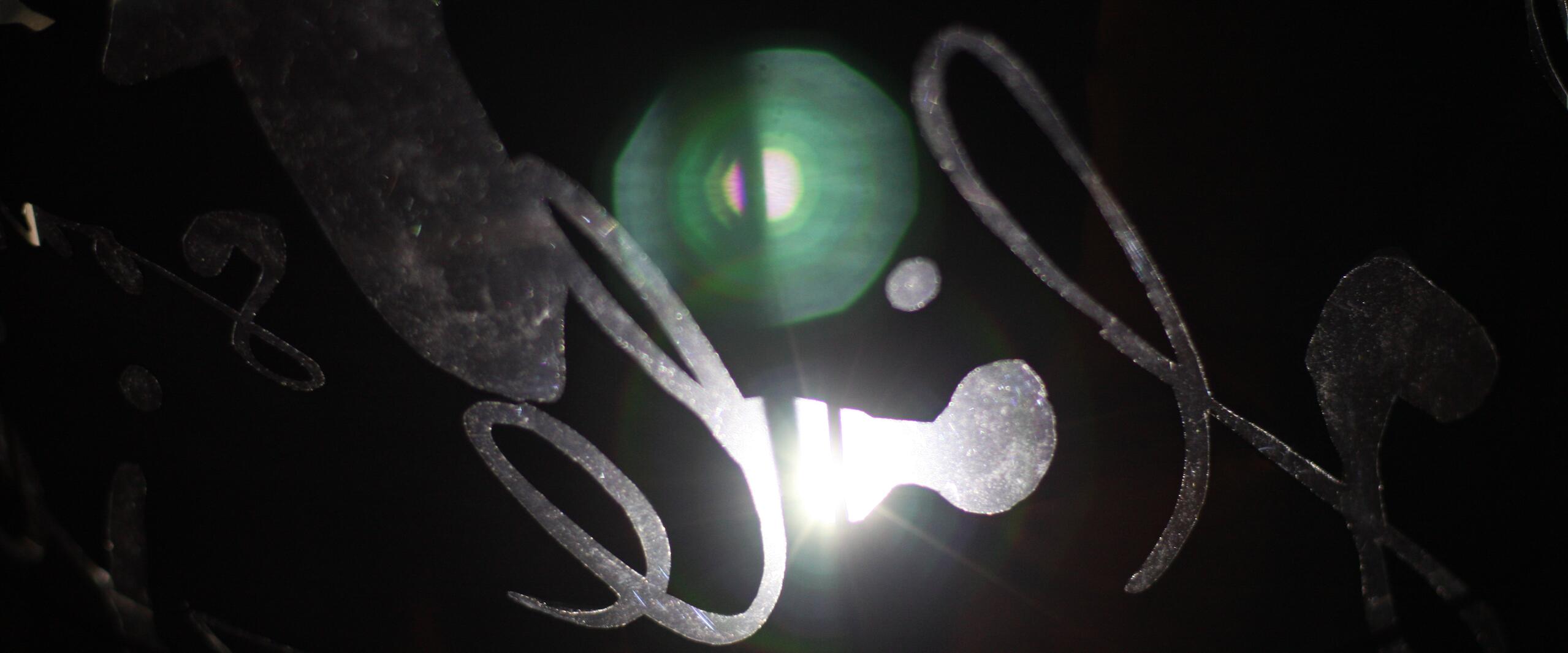 Abstract design with swirling metallic shapes on a dark background, illuminated by a bright central light source, creating a lens flare effect.