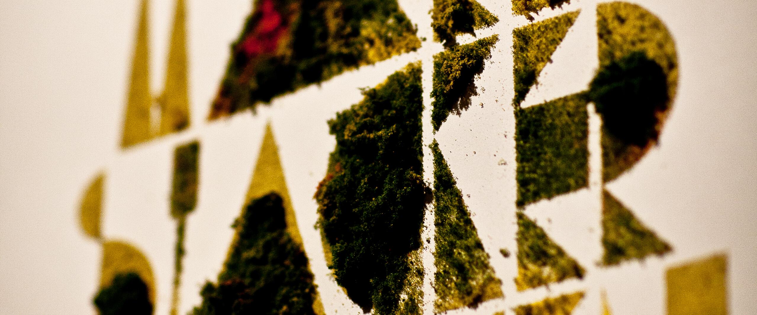 Abstract design with geometric shapes in green and yellow, resembling stenciled moss on a white background.