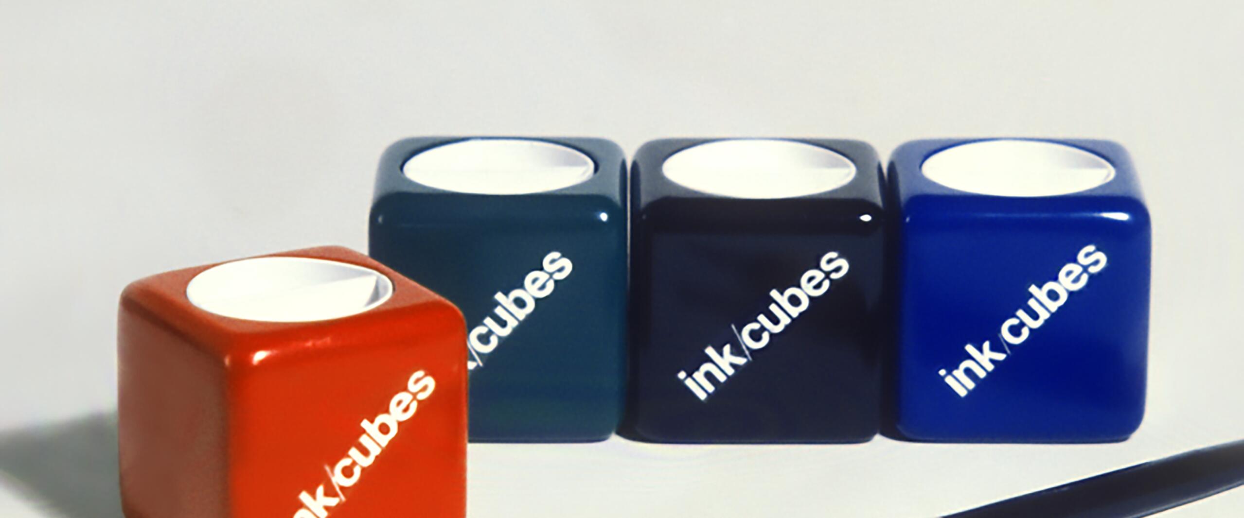 Four colorful ink cubes labeled "ink cubes" in red, teal, black, and blue, arranged in a row. A pen with a nib is in the foreground.