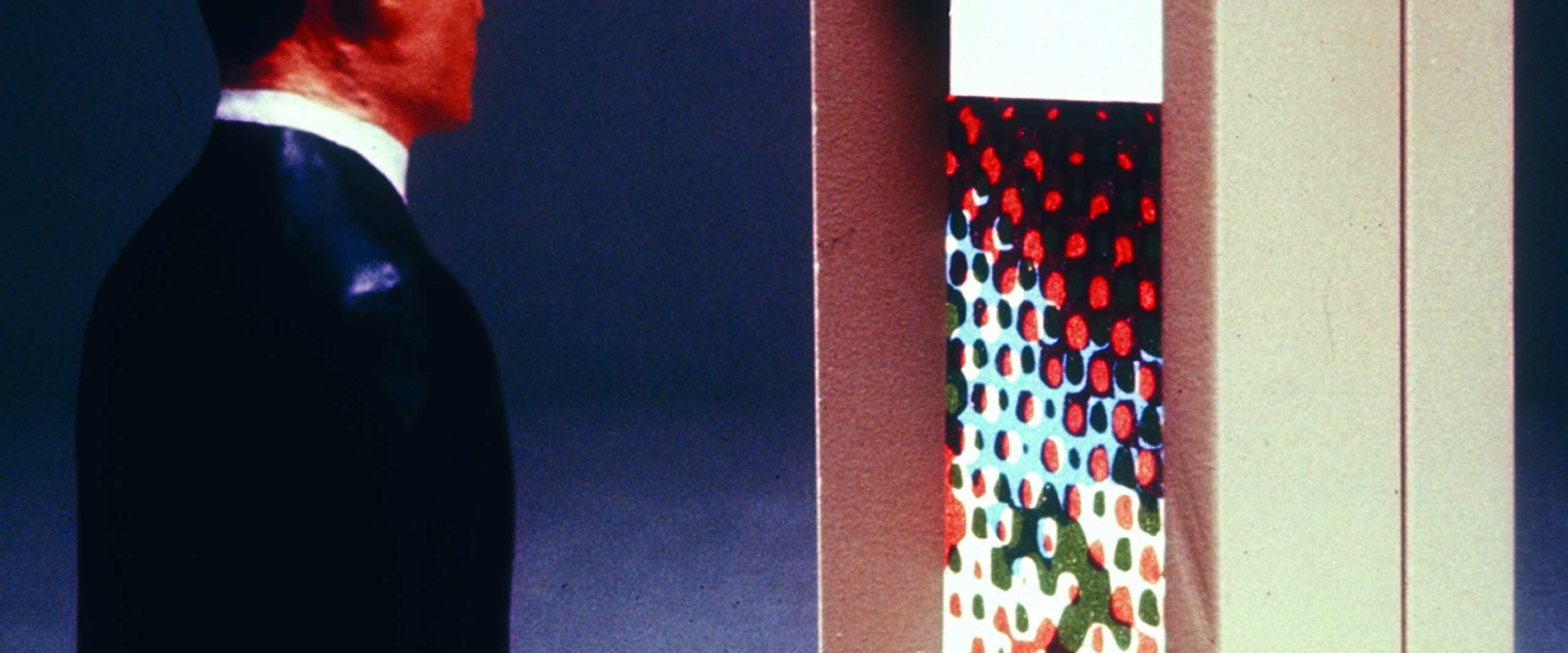 A sculpture of a man in a suit looks at a wall-mounted display with the word "Events" and colorful dots on the screen.