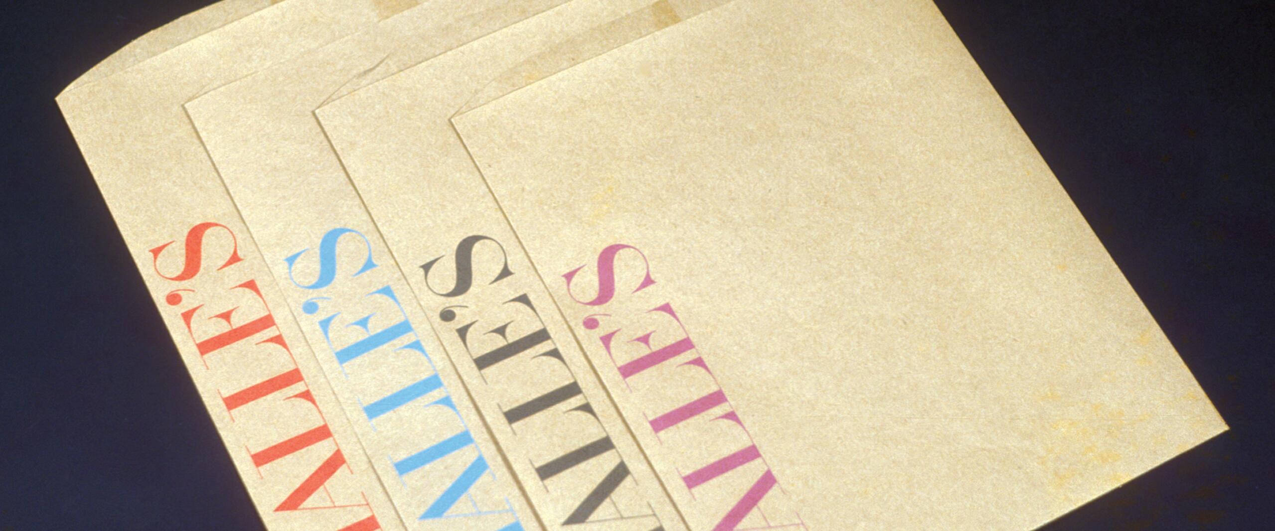 Four beige paper bags each printed with "HALLE'S" in different colors: red, blue, black, and pink, arranged slightly overlapping on a dark background.