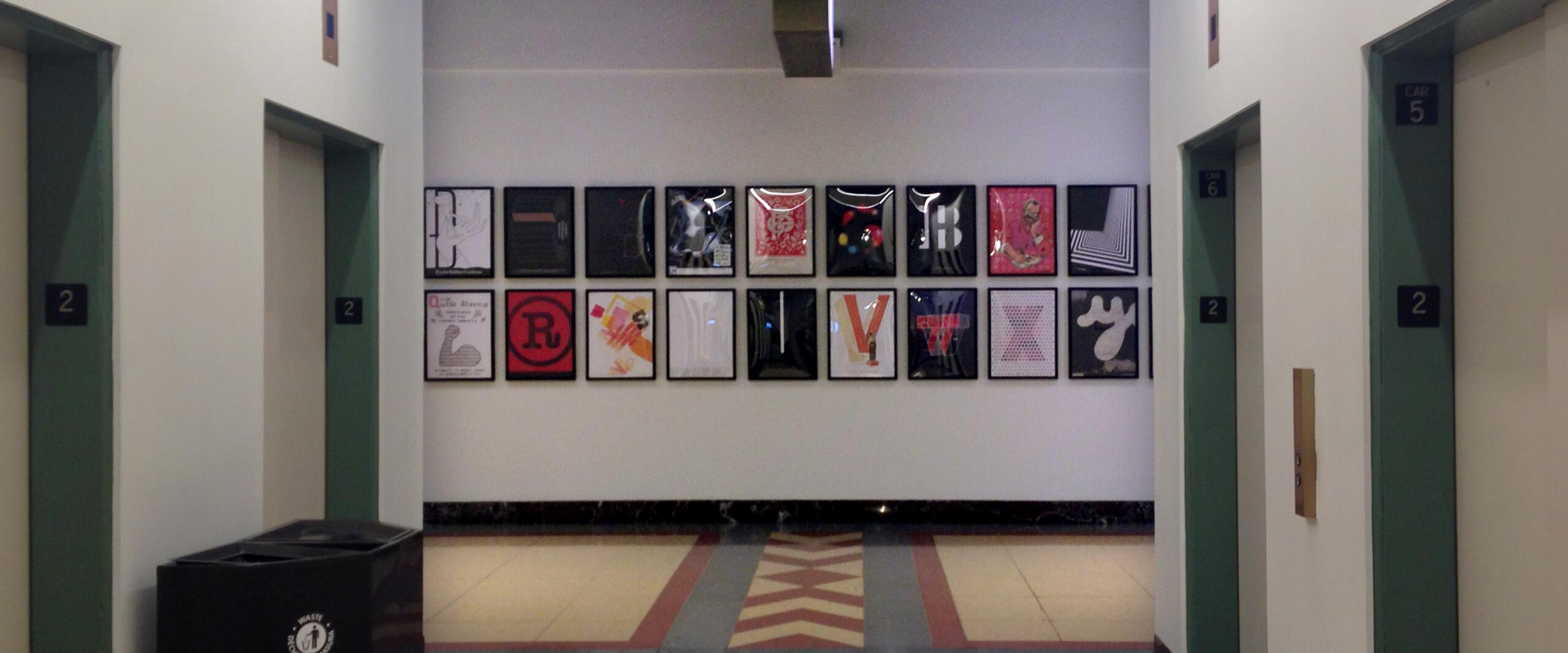 Corridor with elevators on either side, walls decorated with framed colorful artwork.