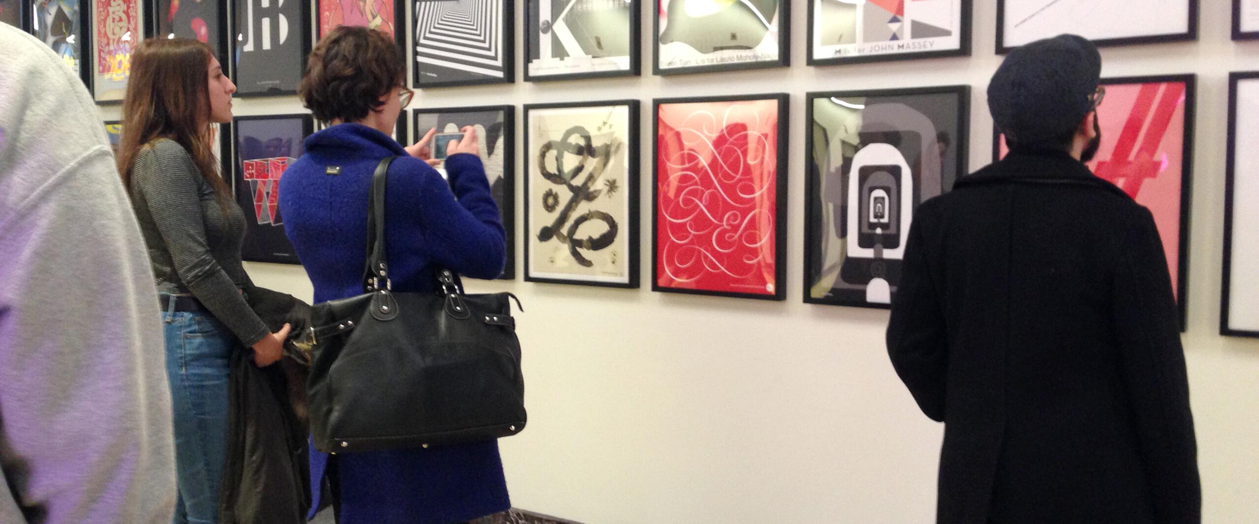 Three people view colorful art prints on a gallery wall.