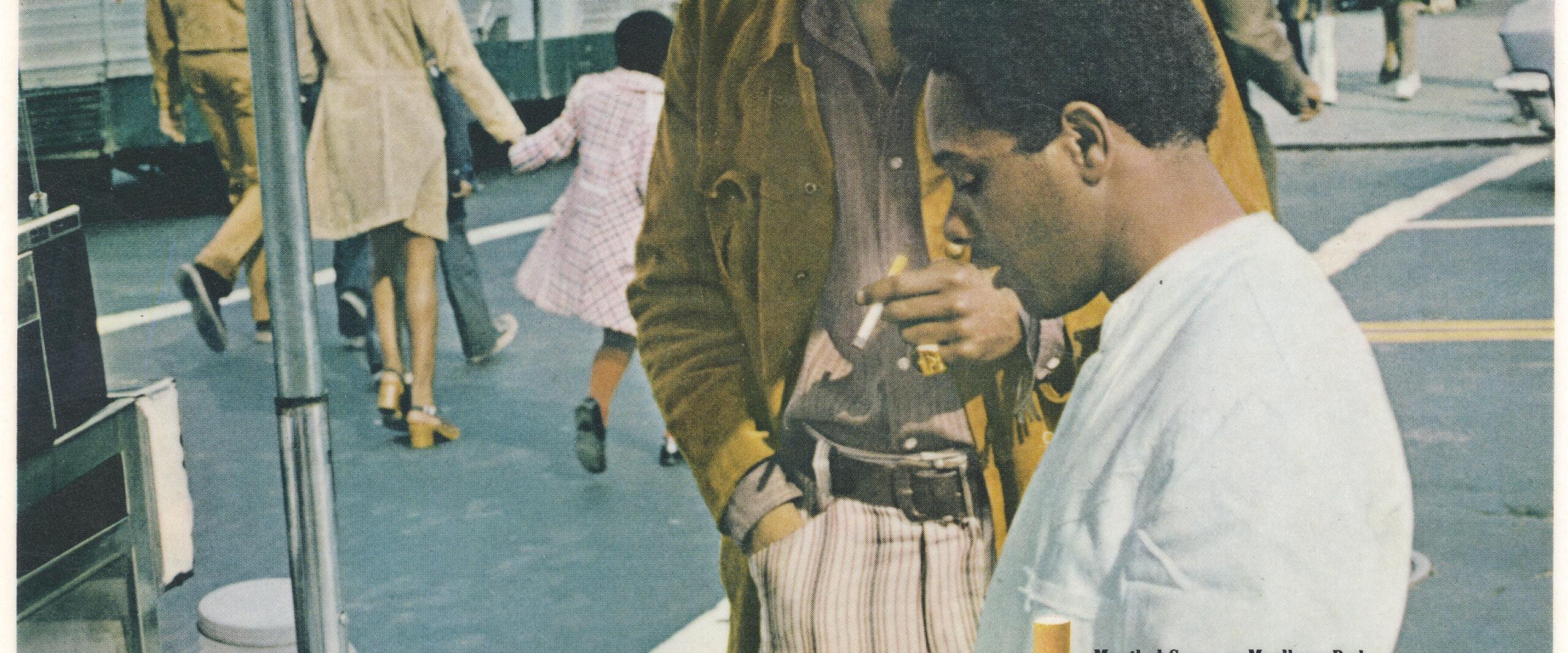 Two men stand at a busy street vendor's cart. One man is handing food to the other. In the foreground are packs of Marlboro cigarettes. The background features a bustling city street with pedestrians and a bus. Text overlays the image.