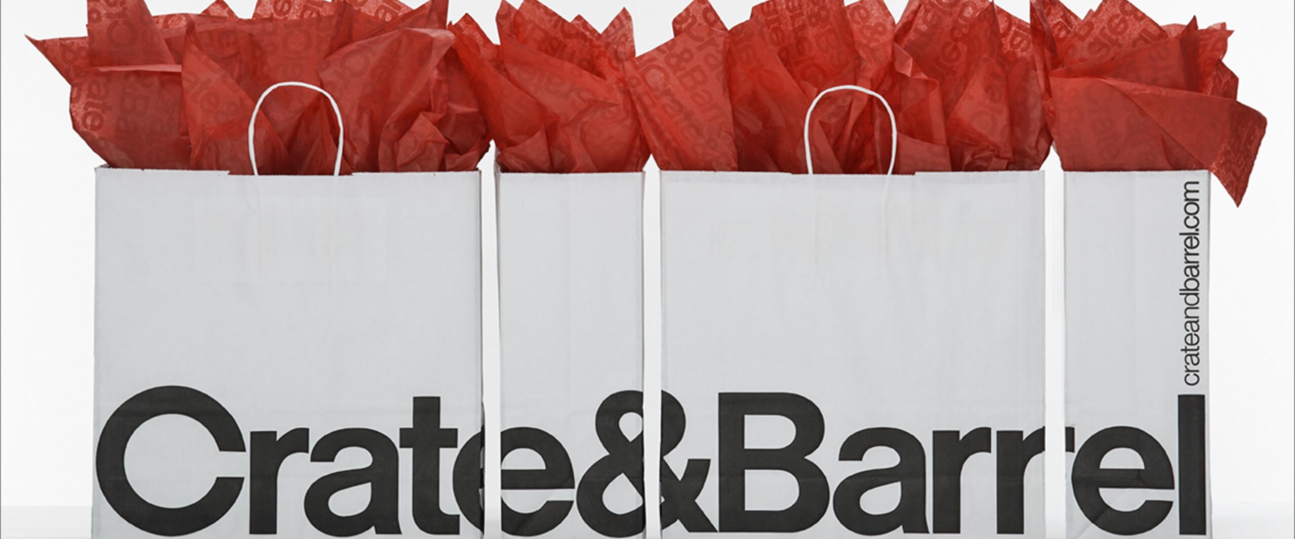 Three Crate & Barrel shopping bags filled with red tissue paper, arranged side by side.