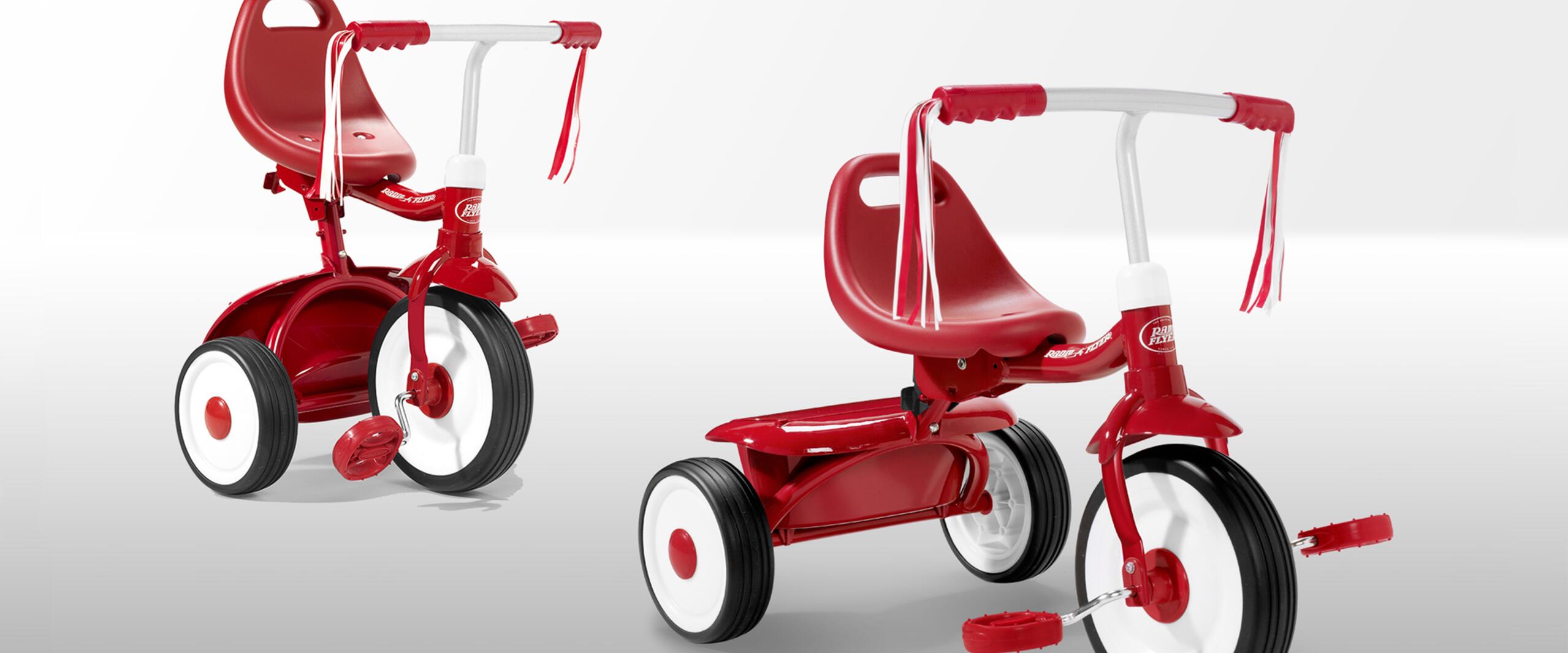 Red and white children's tricycle with streamers on the handlebars, red seat, and large white wheels on a light gray background.