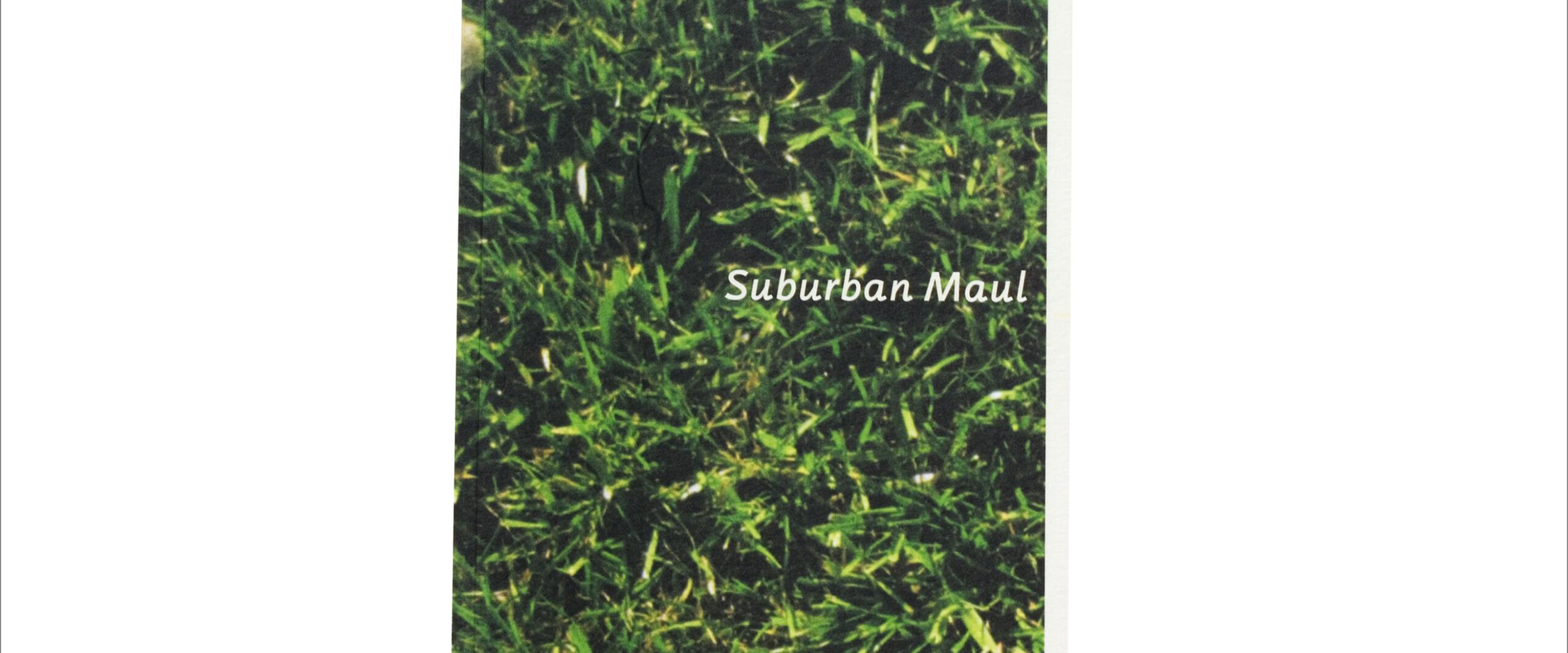 A close-up photograph of green grass with the text "Suburban Maul" in white, set against the grass background.