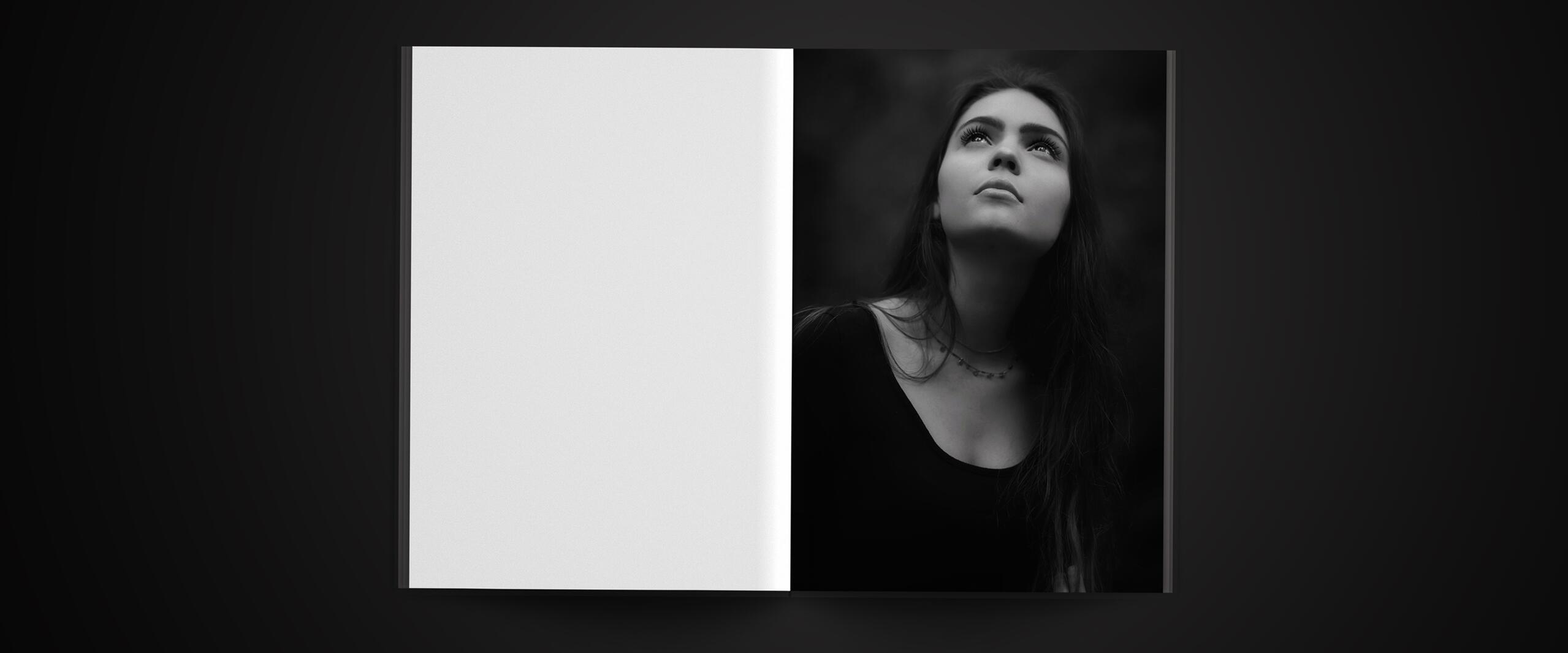 Open book on a dark surface, with a black and white photograph of a woman looking upwards on the right page. The left page is blank.