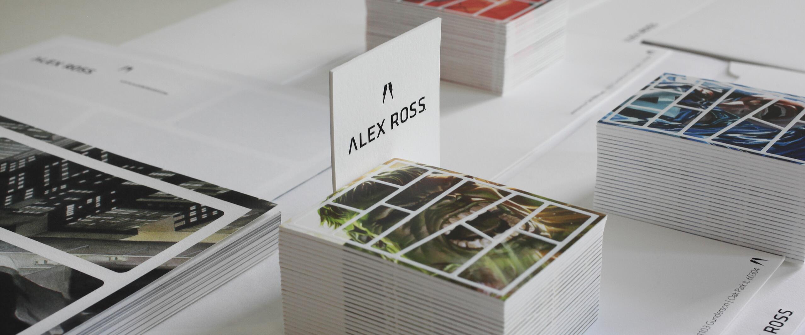Stacks of art cards arranged neatly on a table, featuring colorful illustrations in orange, green, and blue hues. A visible card reads "ALEX ROSS" in black text, with more stacks in the background.