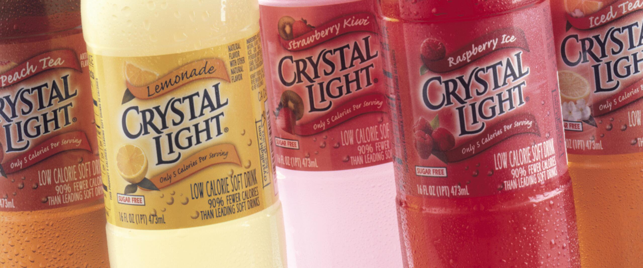 Colorful bottles of Crystal Light drinks with labels displaying flavors like lemonade, strawberry kiwi, and raspberry ice. Each bottle features vibrant colors and condensation droplets, suggesting freshness.