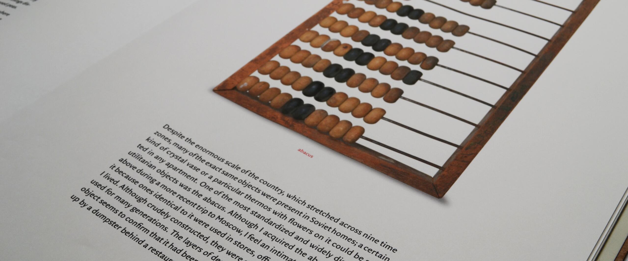 An open book displaying a photograph of a wooden abacus with brown and black beads. The abacus is positioned on the right page, while text is visible on the left and center.