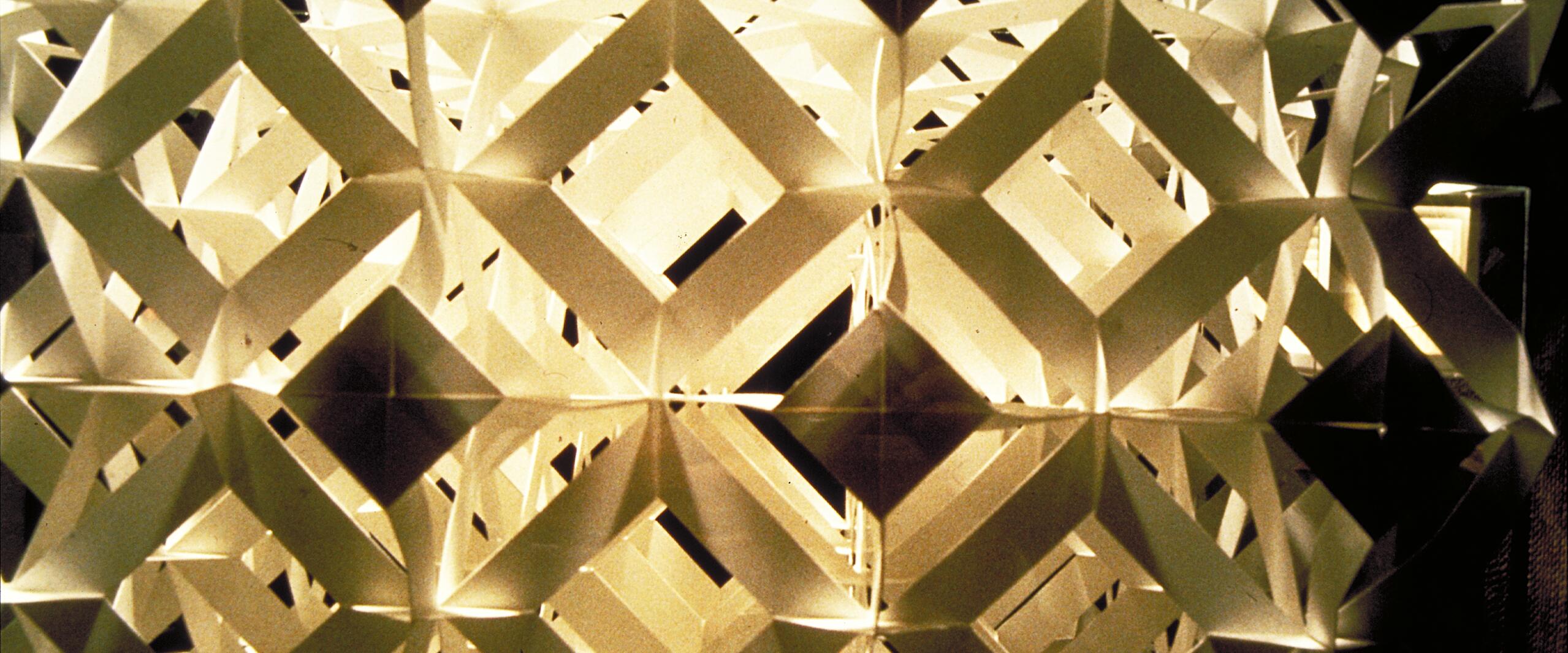 Geometric paper sculpture with interlocking diamond shapes, illuminated from behind, creating intricate patterns and shadows.